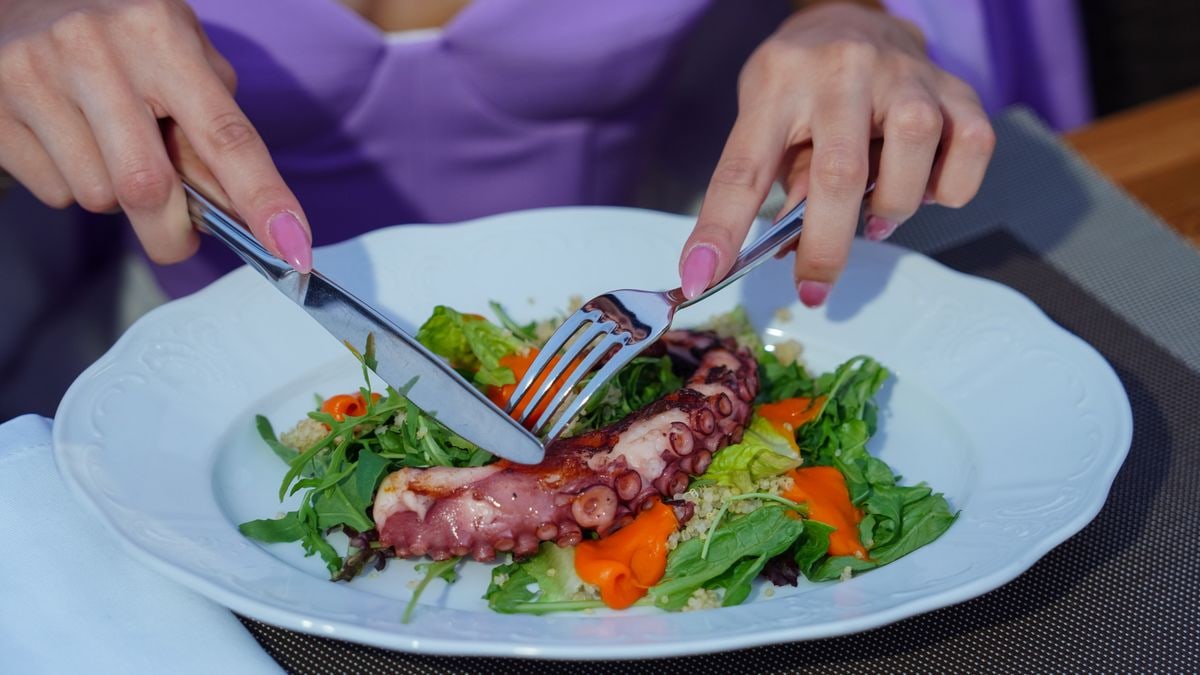 Woman enjoying an octopus salad with fresh greens outdoors. Vibrant and appetizing.